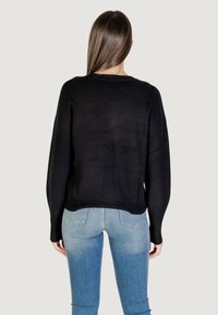Schwarzer Strickpullover mit lässiger Passform, langen Ärmeln und gerippten Bündchen. Getragen über hellblauen, figurbetonten Jeans, die ein einfaches, zeitgemäßes Design zeigen.