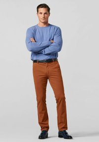 Blauwe trui en bruine chino's, gecombineerd met een zwarte riem en donkere schoenen. De trui heeft een ronde hals, de chino's zijn rechtuit gesneden.