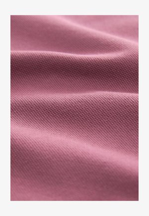 Světle růžová texturovaná tkanina se subtelným vzorem, zobrazující měkké, vlnící se záhyby a hladký povrch.