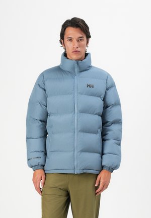 Lichtblauwe pufferjas met hoge kraag, horizontaal gestikt ontwerp, ritssluiting en Helly Hansen-logo op de borst en mouw.