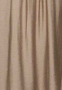 Rideau beige avec de douces pliures verticales et une surface de tissu légèrement texturée, suspendu de manière uniforme.