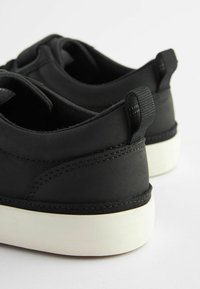 Černé syntetické boty s hladkým povrchem, vybavené bílou gumovou podrážkou a poutkem vzadu; minimalistický design s prošitými akcenty.