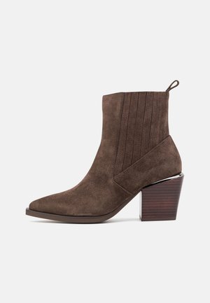 Brązowy zamszowy botek za kostkę z ostrym noskiem, prążkowaną, elastyczną wstawką, pętelką do ściągania i masywnym, układanym drewnianym obcasem.