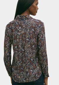 Langarmhemd in Marineblau mit aufwendigem floralen Muster in Creme und Rost. Verfügt über einen hohen Kragen und schmale Manschetten.