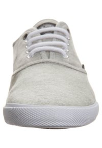Šedé textilní tenisky s nízkým střihem, šněrovacím designem, bílou gumovou podrážkou a texturovanou spodní částí. Mají decentní prošívání a zaoblenou špičku.