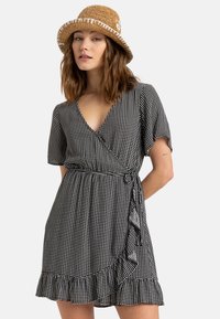 Black and white polka dot wrap dress with short sleeves and ruffled hem. A tan straw hat with white stitching complements the outfit.
