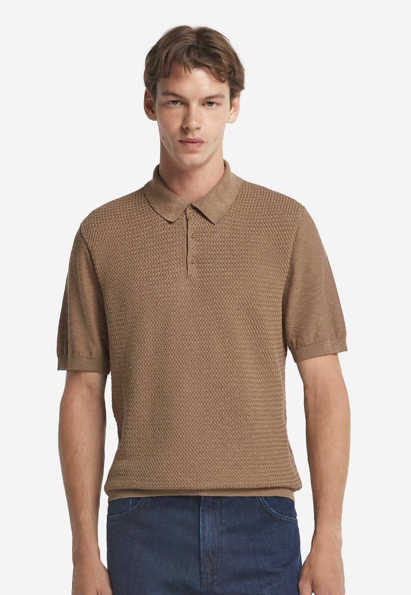 Kortärmad brun polo tröja i texturerad tyg med krage och tre-knappsstängning, matchad med denimjeans.