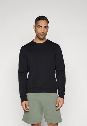 Black sweatshirt with a round neck, long sleeves, ribbed cuffs, and hem. Worn with light green shorts. Smooth texture, minimal design.