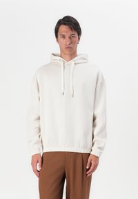 Crème kleurige hoodie van zachte stof, met een geribde zoom en manchetten, verstelbare koorden en een klein geborduurd logo op de borst.
