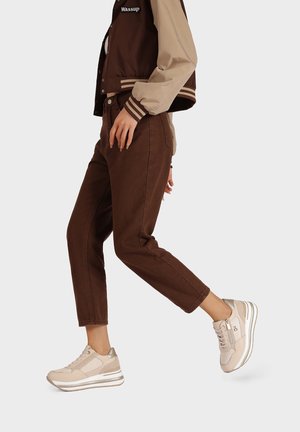Sneaker beige con accenti argentati, lacci marrone chiaro e suola spessa. Abbinati a pantaloni di corduroy marroni e a una giacca marrone-beige.