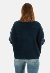 Maglione in misto lana di un blu navy scuro con vestibilità ampia, orlo a coste e maniche larghe, mostrato da dietro, abbinato a jeans azzurri chiari.