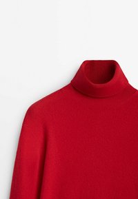 Pull à col roulé rouge en matériau tricot doux. Il présente un col et des poignets côtelés, avec une texture lisse et une silhouette ajustée.