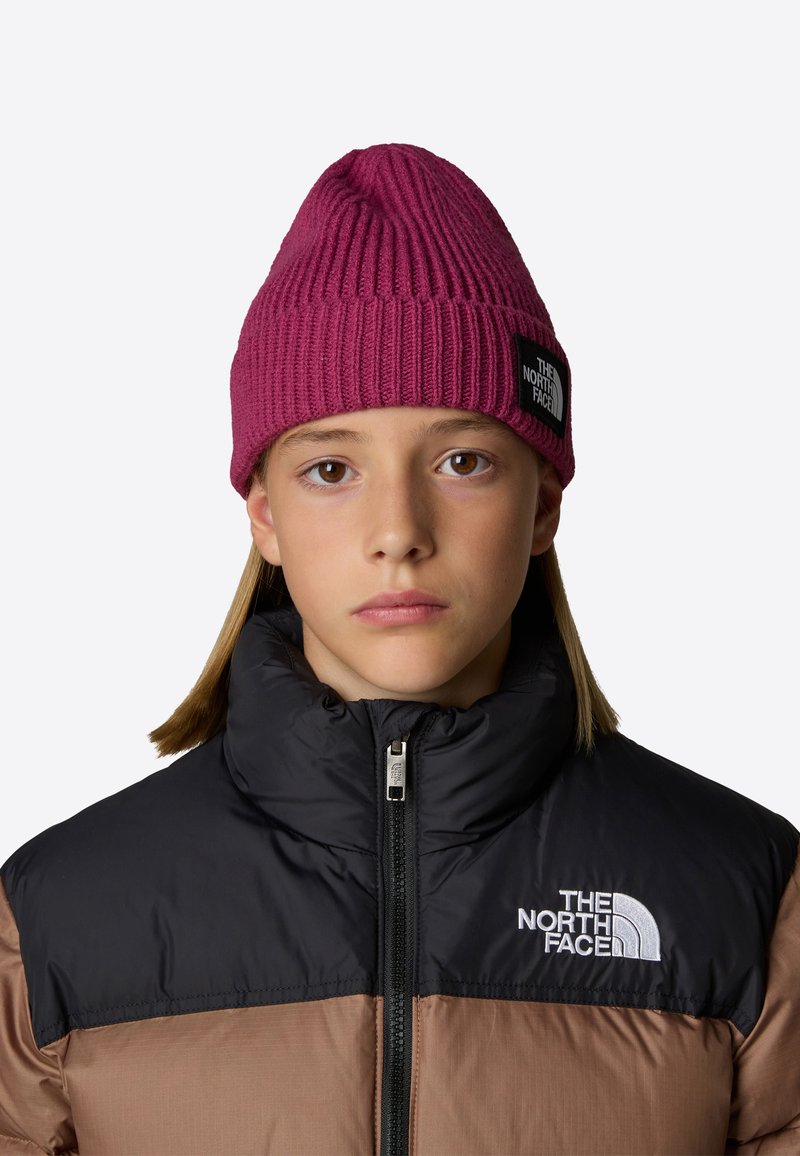 Berretto magenta a coste con design slouchy e patch nero. Indossato con un giubbotto imbottito bicolore con colletto alto e cerniera.