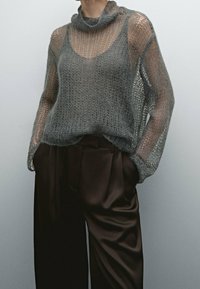 Pull gris clair en maille avec col bénitier et tissage ouvert, associé à un pantalon marron foncé, taille haute, jambes larges.