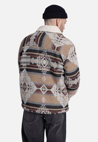 Wollen blend jas met een geometrisch patroon in beige, grijs, rood en zwart. Sherpa-gevoerde kraag; ontspannen pasvorm met rugpand-detail.