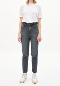 Šedé džíny s vysokým pasem a slim fit, s předními kapsami a zapínáním na knoflík, spárované s bílým tričkem s krátkým rukávem a béžovými teniskami.