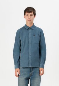 Blue button-up shirt made of textured fabric; features a pointed collar, single chest pocket, and a small label near the pocket.