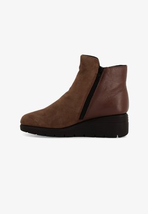 Stivale alla caviglia marrone con finitura scamosciata, zip laterale e tacco a zeppa. Punta arrotondata e suola in gomma nera con grip testurizzato.