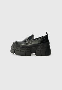 Loafer preto robusto com plataforma grossa, sola texturizada e detalhe de fivela no vamp, nome da marca embutido no meio da sola e laço de puxar no calcanhar.