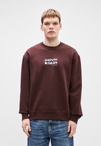 Καφέ φούτερ με ριμπ μανίκια και λαιμό. Λευκό λογότυπο "calvin klein" και κείμενο "New York City" στο στήθος. Μαλακό ύφασμα, άνετη εφαρμογή.