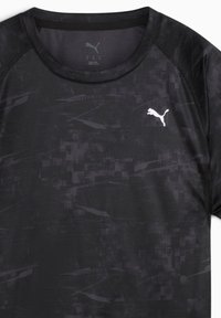 Camiseta deportiva negra con un patrón texturizado. Cuello redondo, mangas raglán y un pequeño logotipo de Puma blanco en el pecho.