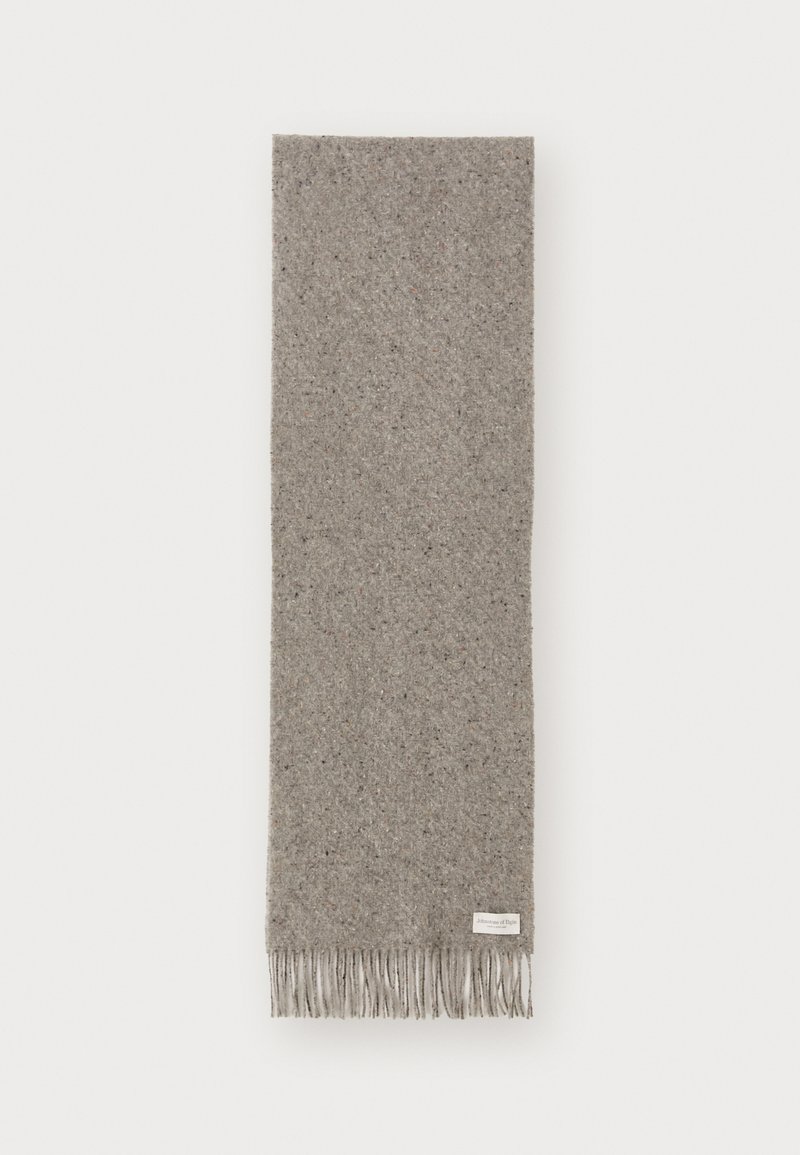 Écharpe en laine de couleur gris clair avec une finition texturée. Présente des bords frangés et une petite étiquette de marque sur un côté.