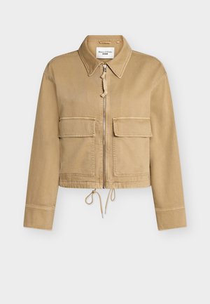 Bež kračeni suknjič z zadrgo spredaj, dvema velikima žepoma s poklopcem, ovratnikom in nastavljivim spodnjim vrvico.