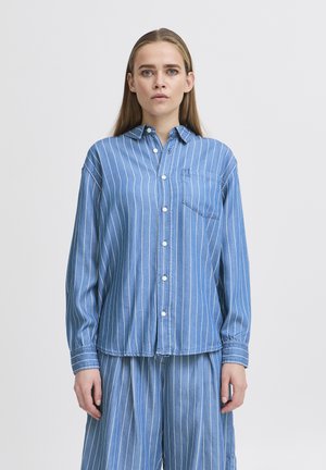 Camicia azzurra chiara, con bottoni, a righe verticali bianche, maniche lunghe e taschino sul petto. Realizzata in denim con una vestibilità rilassata.