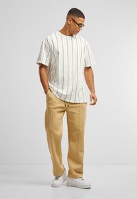 Hvit T-skjorte med korte ermer og svarte vertikale striper, sammen med beige joggebukser og hvite sneakers. Enkelt og uformelt design.