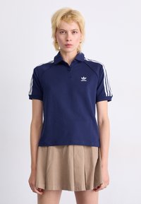 Polo shirt bleu marine avec col, présentant des accents blancs à trois bandes sur les épaules et un logo brodé sur la poitrine.