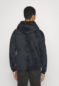 Tmavě modrá mikina s kapucí ve stylu tie-dye, s přední kapsou typu kangaroo, žebrovanými manžetami a spodním lemováním, velkou kapucí a volným střihem.