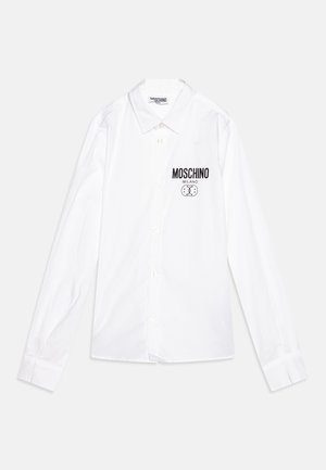 Hvid, langærmet skjorte lavet af bomuld. Har en button-down krave og et sort Moschino-logo med et tegneserieansigt på venstre bryst.