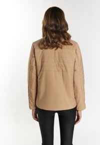 Beige gewatteerde jas met een gladde textuur, verlaagde schouders en een rechte snit. Gecombineerd met zwarte fitted broeken.