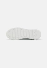 White sneaker sole featuring a textured rubber design with horizontal and vertical grooves for grip, embossed logo detail on the heel.