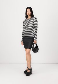 Zwart-witte gestreepte lange mouwtop gecombineerd met een zwarte leren mini-rok. Model houdt een zwarte tas vast en draagt opvallende zwarte plateau schoenen.