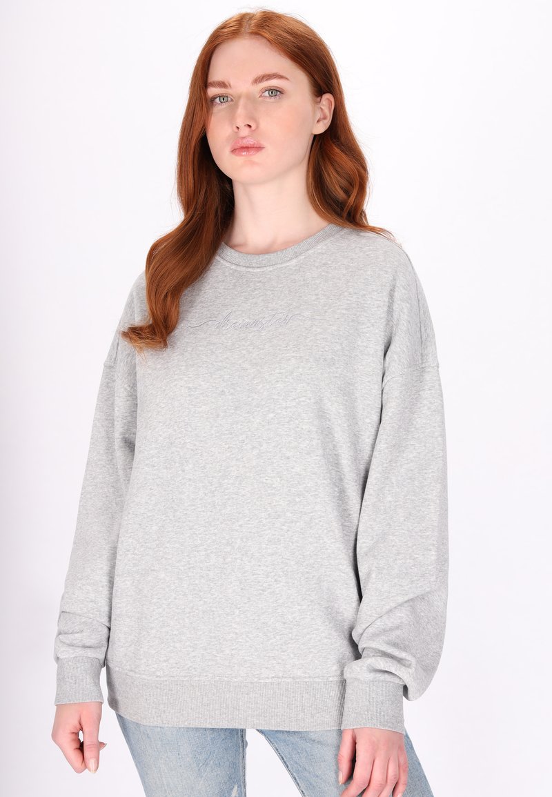 Světle šedá oversized mikina vyrobená z měkké bavlněné směsi. Má kulatý výstřih, žebrované manžety a nenápadný vyšívaný detail na hrudi.