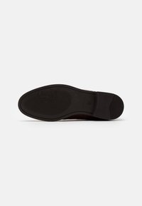 Semelle de chaussure en caoutchouc noir avec motif de grip texturé ; présente un logo embossé au centre et un bord lisse.