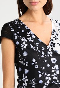Vestido negro con estampado floral en tonos azul y blanco, con un diseño de escote en V, mangas negras texturizadas y una textura de tejido suave y ligero.