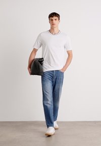 Hvid t-shirt med sort krave, lyseblå jeans og hvide sneakers. Modellen bærer en sort tote taske med en glitrende finish.