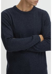 Sweater bleu marine foncé en maille texturée, avec un col rond et des poignets côtelés. Le design est simple et classique.