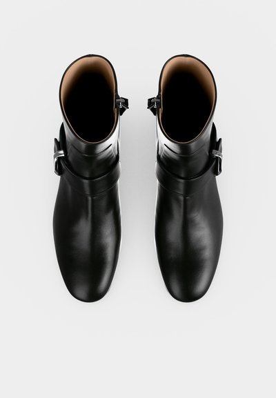 Bottes courtes en cuir noir avec boucles latérales vues de dessus sur fond blanc.