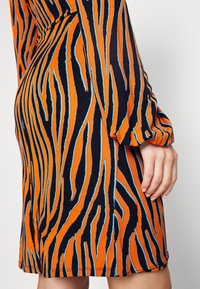 Robe à manches courtes de couleur orange vif avec des rayures zébrées noires et bleues, présentant une silhouette ajustée et un tissu lisse et extensible.