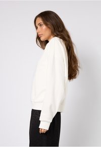 Felpa oversize color crema con maniche lunghe e polsini a costine, realizzata in tessuto morbido, abbinata a pantaloni neri con stampa leopardata.