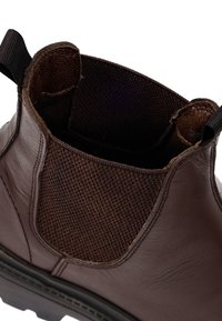 Bruine leren enkellaars met een gestructureerde, bruine elastische zijpaneel, trekband en stevige zwarte zool. Het interieur heeft een zachte voering.