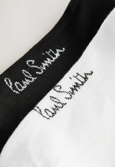 Primer plano de calcetines blancos y negros con el logo "Vans Skate" bordado cerca del área del tobillo.