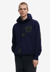 Marineblauwe hoodie met trekkoord, voorzien van groene dierenontwerpen op de voorkant en mouwen. Zware stof met een buidelzak.