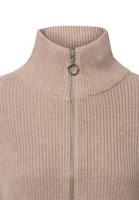 Maglione lavorato a maglia beige con colletto alto e zip argentata, caratterizzato da una texture a coste e dettagli di cucitura ben evidenti.