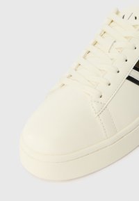 Beli usnjeni športni čevlji z ravnimi vezalkami, zaobljenim nosom in kontrastnimi črnimi črtami ob strani. Gladka površinska tekstura in gumijast podplat.