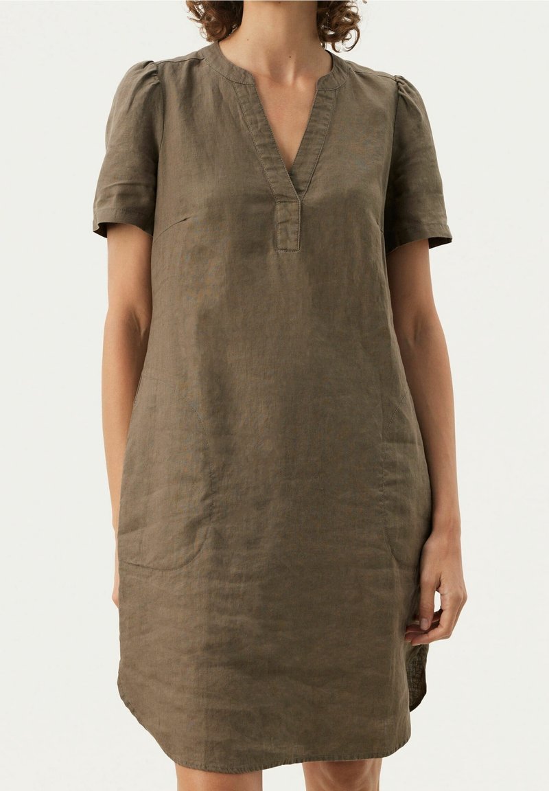 Personne portant une robe en lin marron à manches courtes avec un col en V et des épaules légèrement bouffantes sur un fond uni clair.