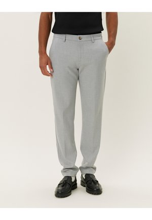 Lichtgrijze, op maat gemaakte broek met een gladde textuur, slim fit en een enkele knoopsluiting. In combinatie met zwarte instappers voor contrast.